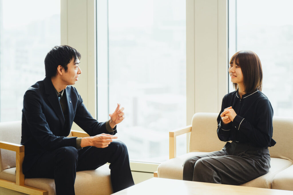 ソファに座り向き合ってジェスチャーを入れながら話すトレーナーとトレーニーの様子